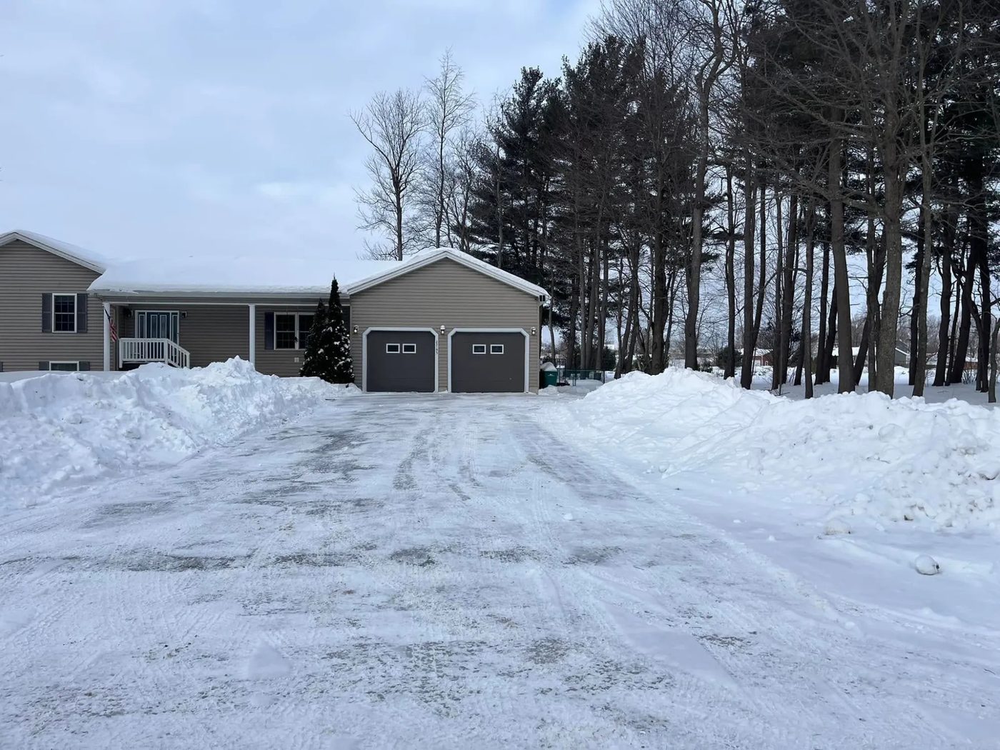 A driveway plowed down to bare pavement in front of a two-car garage, with snow banked high on both sides